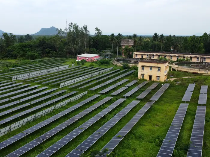 Aerial view of a large ground-mounted solar farm with rows of panels beside a facility